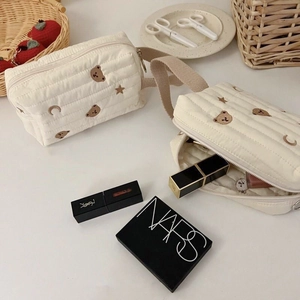 Creamy white quilted makeup bag with bear embroidery and beige woven strap handle