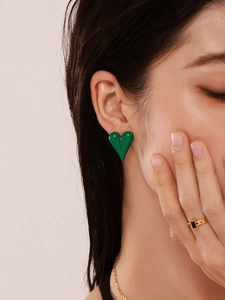 Close-up of a model wearing emerald green heart stud earrings and a gold black ring