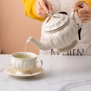Pouring tea from an embossed ceramic pot into a white vintage teacup on marble table