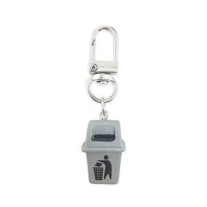 Close-up of a creative grey mini trash can keychain with metal hook on white background