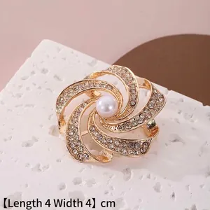 Détail macro d'une broche spirale dorée de 4cm avec une perle blanche et strass