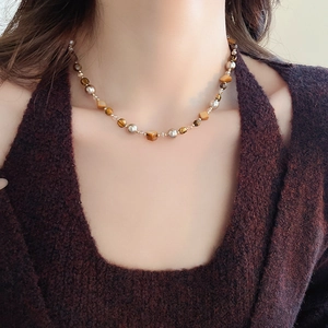 Detail einer Perlenkette mit Tigeraugen und Perlen an einem Modell in braunem Strick