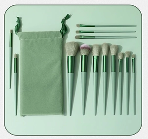 Flat lay of 12 green gradient makeup brushes and velvet pouch on a soft green background