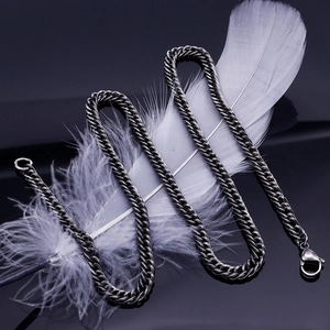 Artistic close-up of dark silver Cuban chain necklace next to a white feather