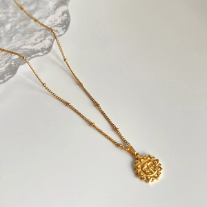 Gros plan du pendentif soleil en acier plaqué or 18 carats sur chaîne à perles sur glace