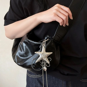 Detail of a crescent black leather shoulder bag featuring a silver starfish charm and chain