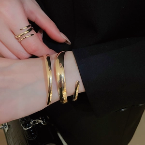 Detail view of a polished gold hollow spiral cuff bracelet on a black blazer sleeve