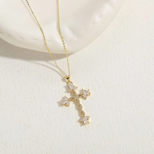Macro detail of golden cross pendant featuring marquise-cut zircons on a white background