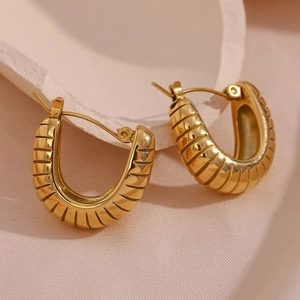 Close-up of golden U-shaped earrings with textured surface on a soft fabric base