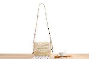 Detail of a beige woven shoulder bag with wooden beads on light wood surface