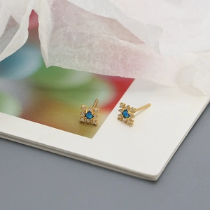 Macro shot of gold snowflake earrings with a deep blue gemstone and small white diamonds
