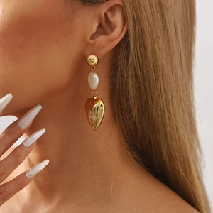 Golden heart drop earrings with imitation pearls worn by model in a stylish close-up shot