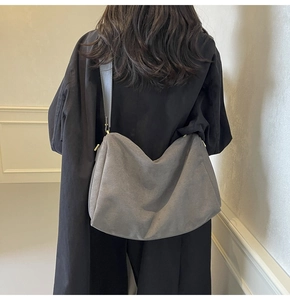 Gray faux suede hobo bag with wide shoulder strap shown on model against a beige wall