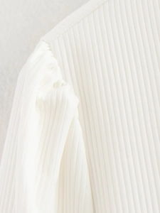 Detail of white rib-knit fabric texture with precise shoulder stitching and pleated cuffs