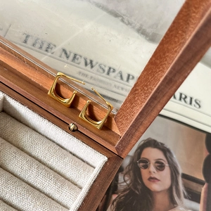 Close-up of minimalist square gold earrings displayed on a rustic wooden jewelry box