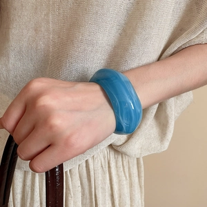 Detail of blue acrylic cuff bracelet with marble texture worn on model wrist