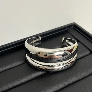 Close-up of a silver double-layer wavy metal cuff bracelet on a black leather tray