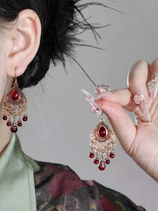 Macro detail of retro bronze waterdrop earrings with red beads and hollow pattern
