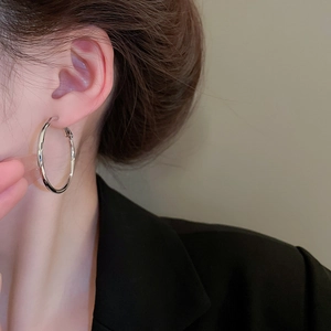 Close-up of a large polished silver hoop earring worn by a model in black blazer
