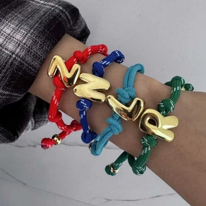 Nahaufnahme bunter geflochtener Seilarmbänder mit klobigen 18 Karat vergoldeten Buchstabenanhängern