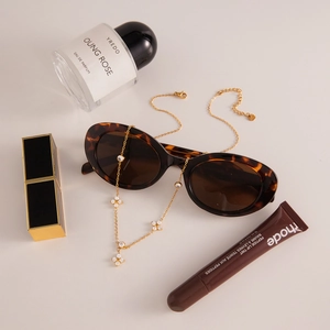 Close-up of golden clover necklace with zircons next to tortoiseshell sunglasses