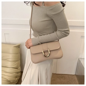 Detail of the golden D-ring buckle on a beige leather baguette bag worn by a model