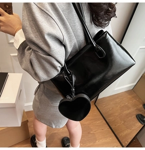 Polished black patent leather tote bag with heart charm shown on model in studio