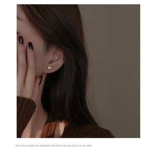 Close-up of minimalist heart stud earring in mirror-finish silver worn by a model