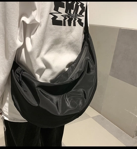 Side view of black nylon crescent crossbody bag worn with a casual streetwear outfit