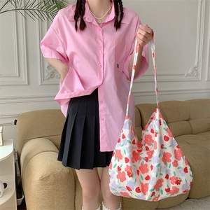 Floral canvas tote bag carried by model wearing pink shirt and black pleated skirt