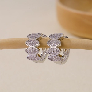 Close-up of silver earrings with pave-set zircons hanging on a natural wooden branch