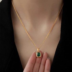 Collier élégant en acier titane doré avec pendentif émeraude rectangulaire porté par un mannequin