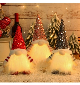 Close-up of three glowing Christmas gnomes with sequin hats and LED lights in a cozy setting