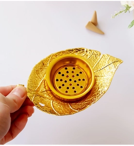 Detailed close-up of a golden leaf-shaped metal incense burner held by a hand