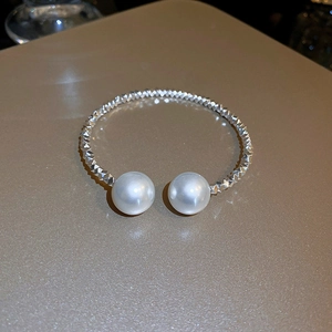 Macro detail of silver open choker necklace with large white pearls on a beige surface