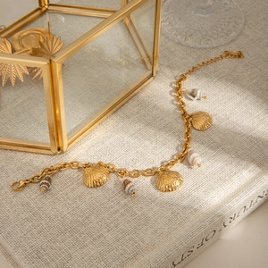 Detail of gold chain bracelet featuring natural conch and metallic shell charms on a book