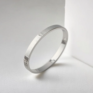 Macro detail of silver stainless steel bangle with etched wave pattern on white texture