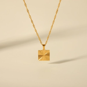 Detailed close-up of a square gold pendant necklace with a radiant textured design