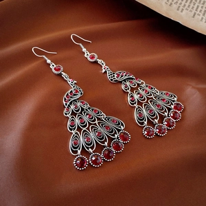 Macro detail of bohemian peacock drop earrings with red rhinestones on silk