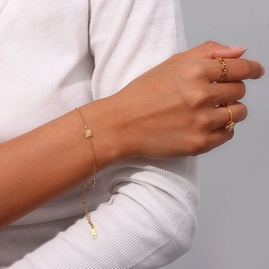 Close-up of 18K gold plated thin bracelet with square pendant and chain rings on hand