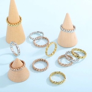 Three-color twisted rope rings in gold, silver, and rose gold on wooden display stands