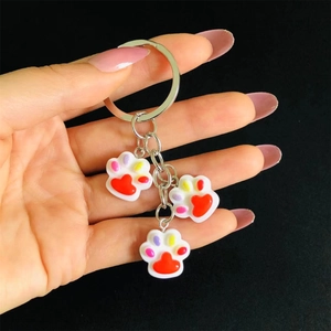 Detail of colorful resin cat paw charms on a metal keychain held against black background