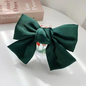 Détail d'une pince à cheveux à gros nœud en satin vert foncé au fini soyeux et poli