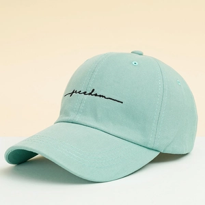 Detail of mint green cotton baseball cap featuring black freedom cursive embroidery