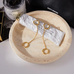 Détail de boucles d'oreilles chaînettes dorées avec cercles en zircon sur accessoires blancs