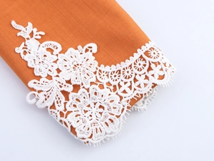 Close-up of elegant white lace trim on orange cotton linen fabric of short blazer jacket