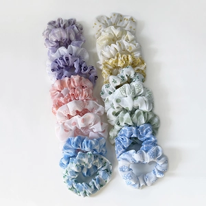 Floral and checkered fabric scrunchies in purple, pink and blue on white background