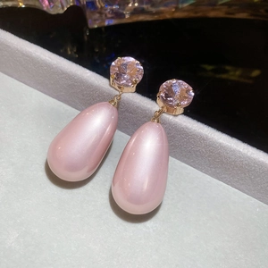 Macro detail of elegant pink teardrop pearl earrings with diamond accents on velvet