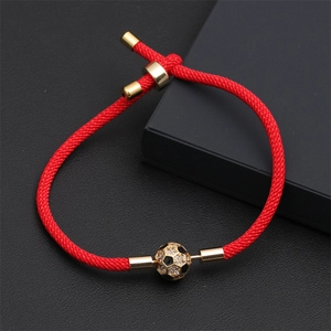 Dettaglio di bracciale intrecciato rosso con ciondolo a pallone da calcio dorato e cristalli