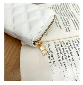 Close-up of golden metal zipper and quilted stitching on a white patent leather wallet